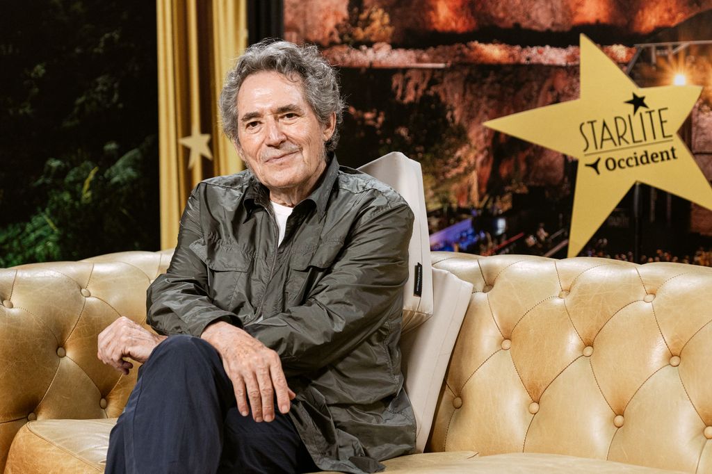 Miguel Ríos sonríe en un sofá con una estrella de Starlite al fondo.