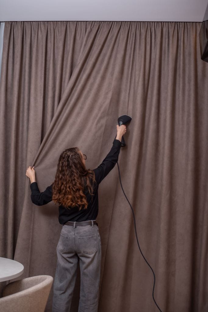 Mujer limpiando las cortinas con vapor.