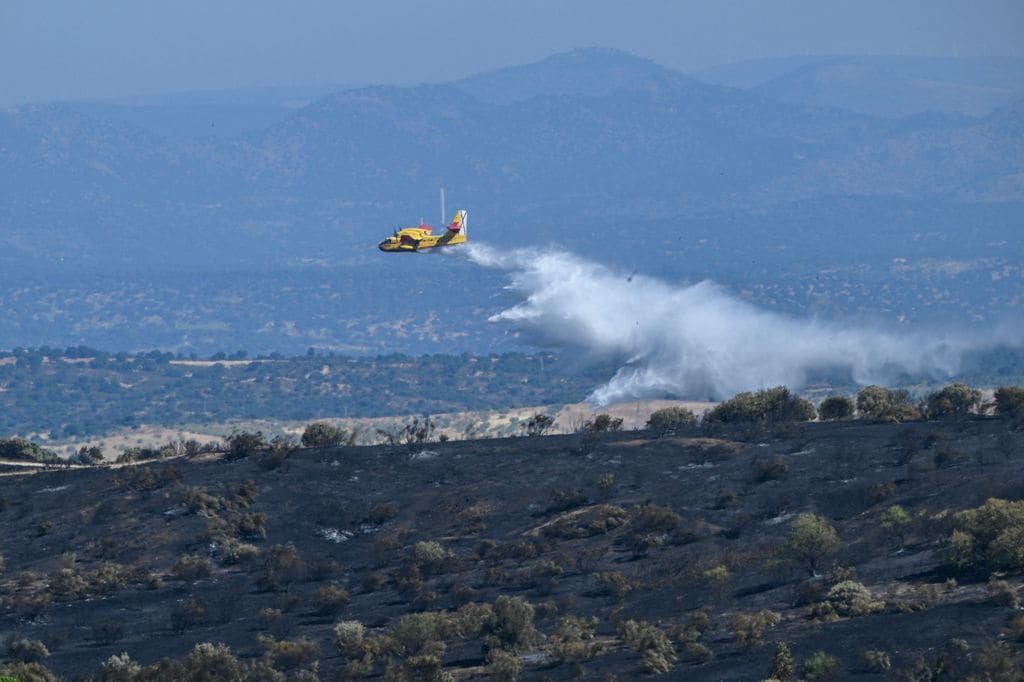 Un avión de extinción de incendios lanza agua sobre las zonas quemadas tras un incendio forestal que se inició en el municipio de Mentrida (Toledo)