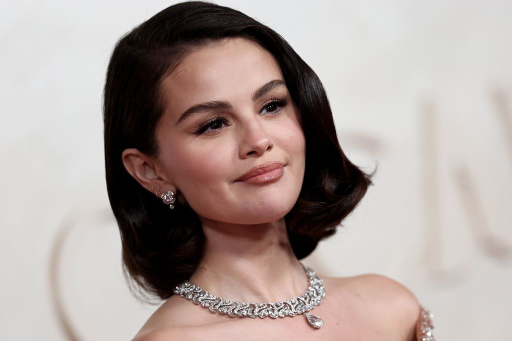 Selena Gomez con peinado al estilo old Hollywood y joyas brillantes, posando en una alfombra roja.