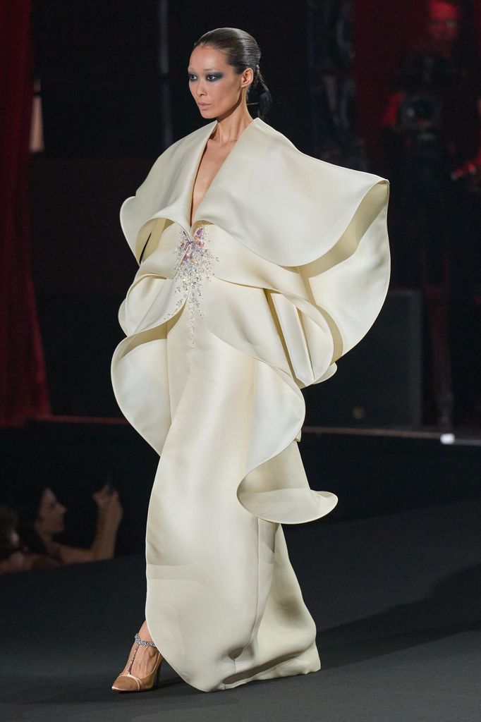Modelo en pasarela con vestido blanco de mangas anchas y tacones dorados.