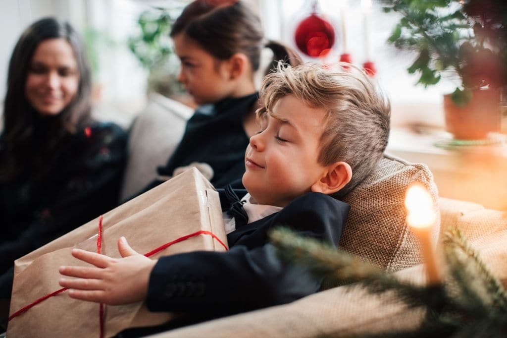 Niño sonriendo tumbado en el sofá del salón con un regalo de Navidad entre las manos.
