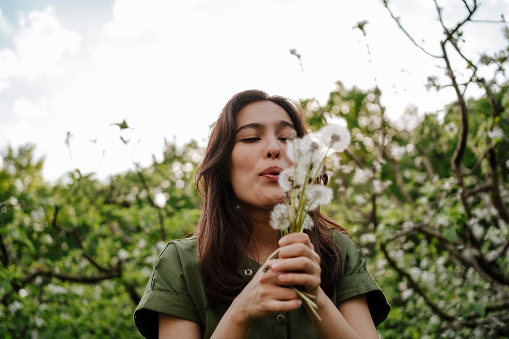 mujer soplando dientes de león en primavera, al aire libre