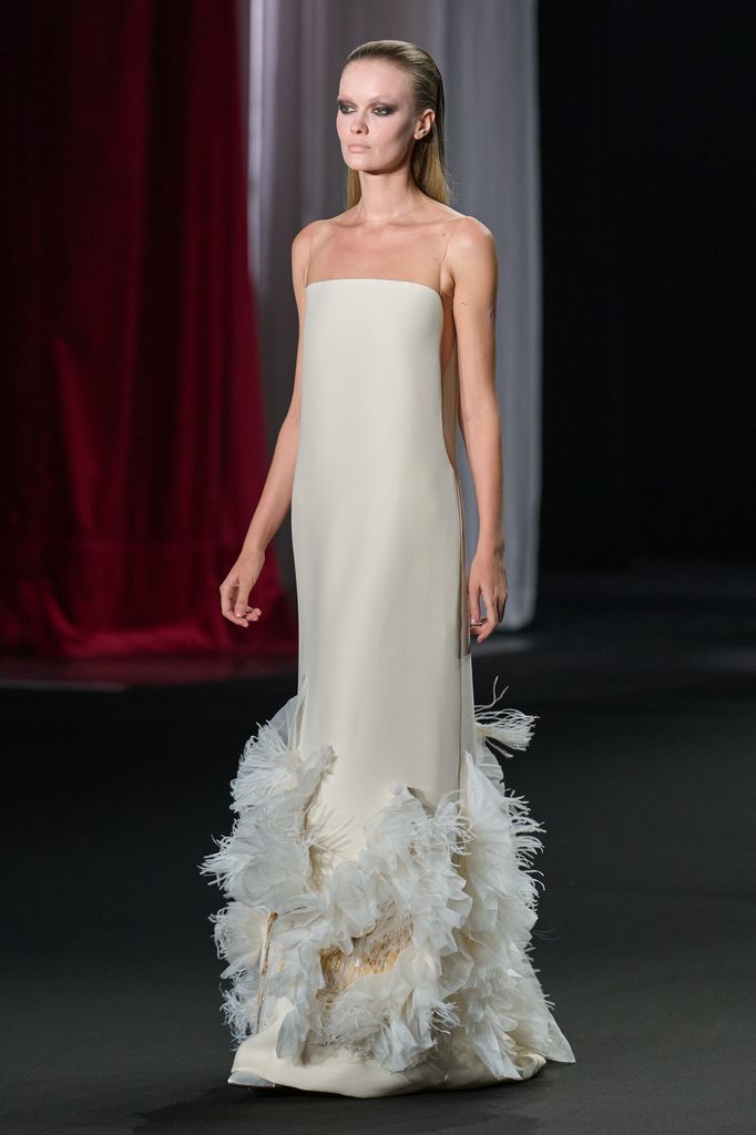 Modelo en pasarela con vestido blanco de plumas en desfile de moda.