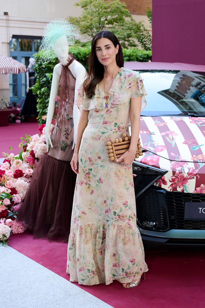 Mujer en vestido floral posa junto a maniquí y auto decorado con flores.
