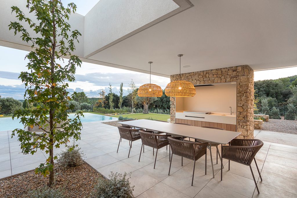Porche con piscina y cocina exterior integrada pared de piedra, mesa, sillas y lámparas de fibras vegetales