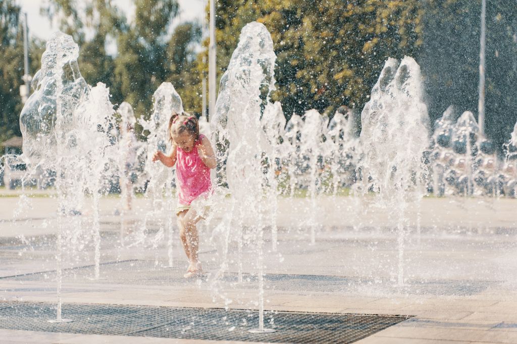 Niña jugando con los chorros de una fuente pública
