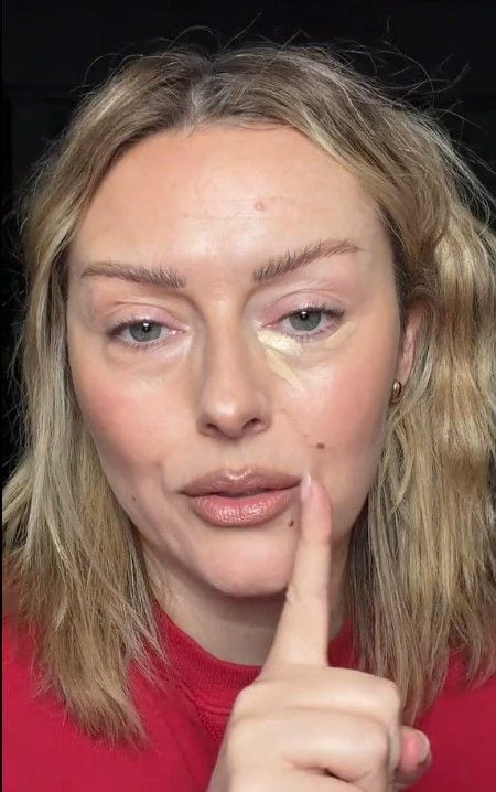 Katie Jane Hughes con jersey rojo aplicando el corrector de ojeras