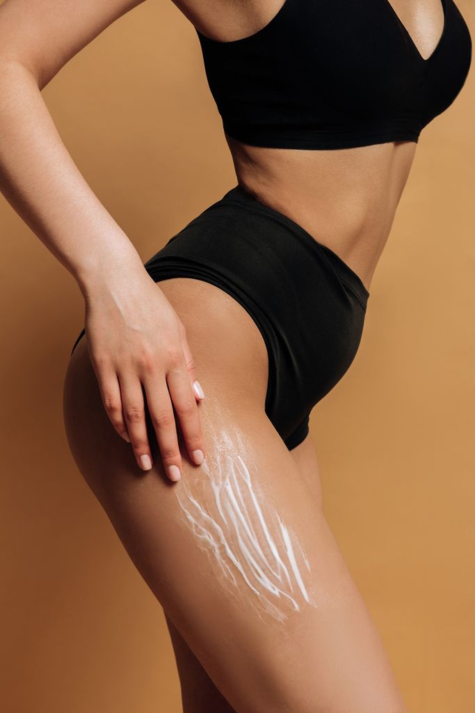 Cuerpo de mujer con bikini negro de talle alto y crema en el muslo