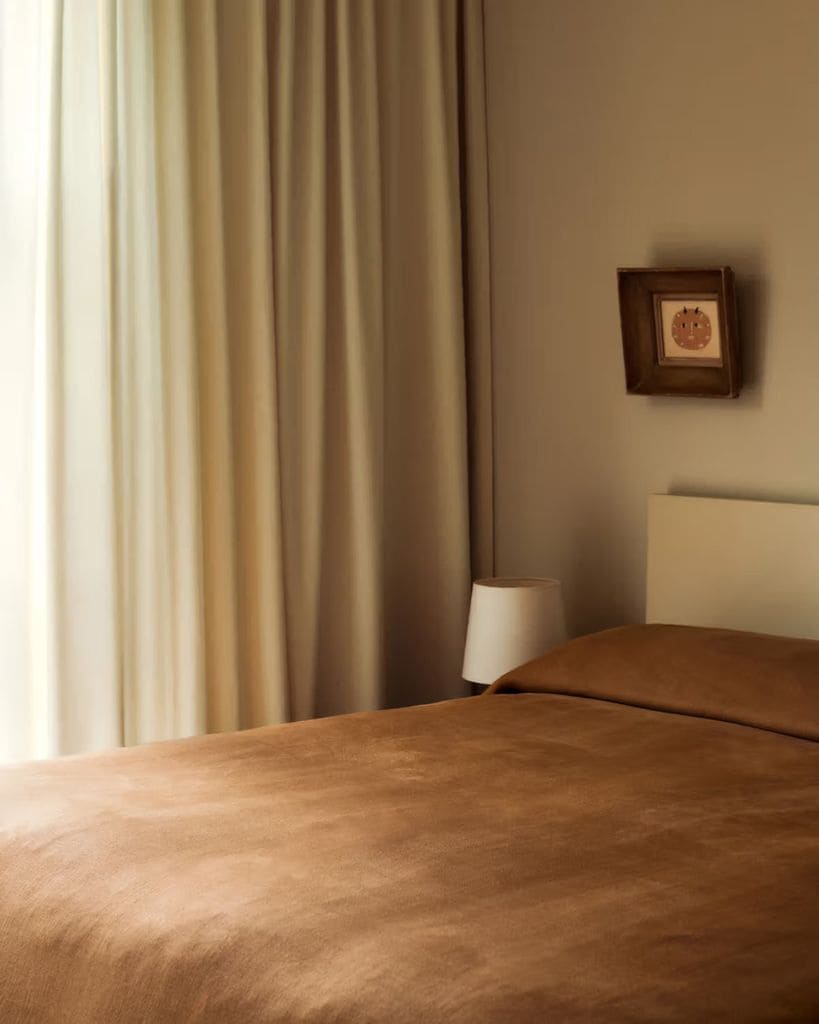 Dormitorio con cortinas crudas y colcha marrón