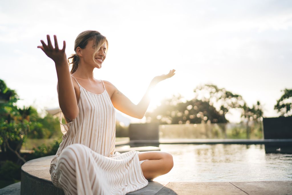 mujer sonriente haciendo yoga y meditación junto a una piscina 