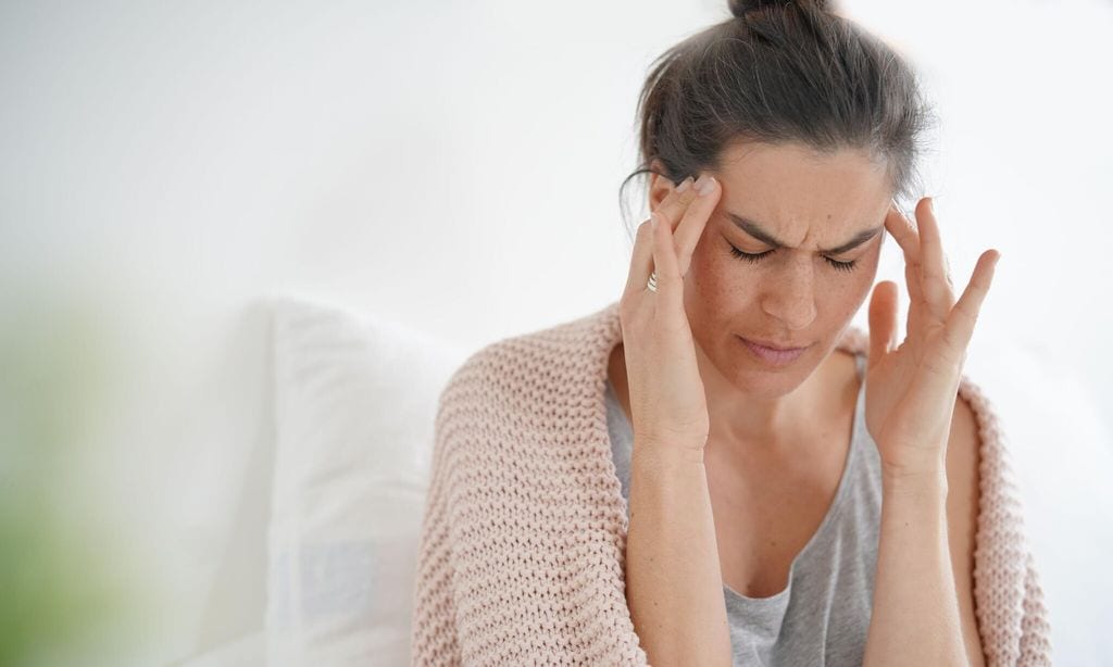 mujer con las manos en las sienes con dolor de cabeza