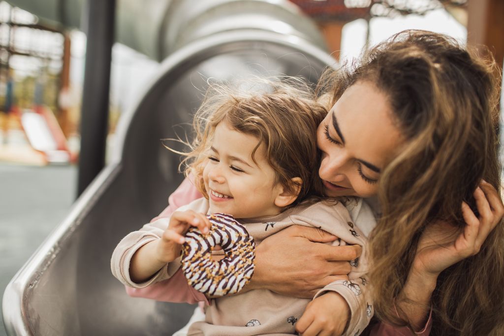 Madre con su hija pequeña en un tobogán felices
