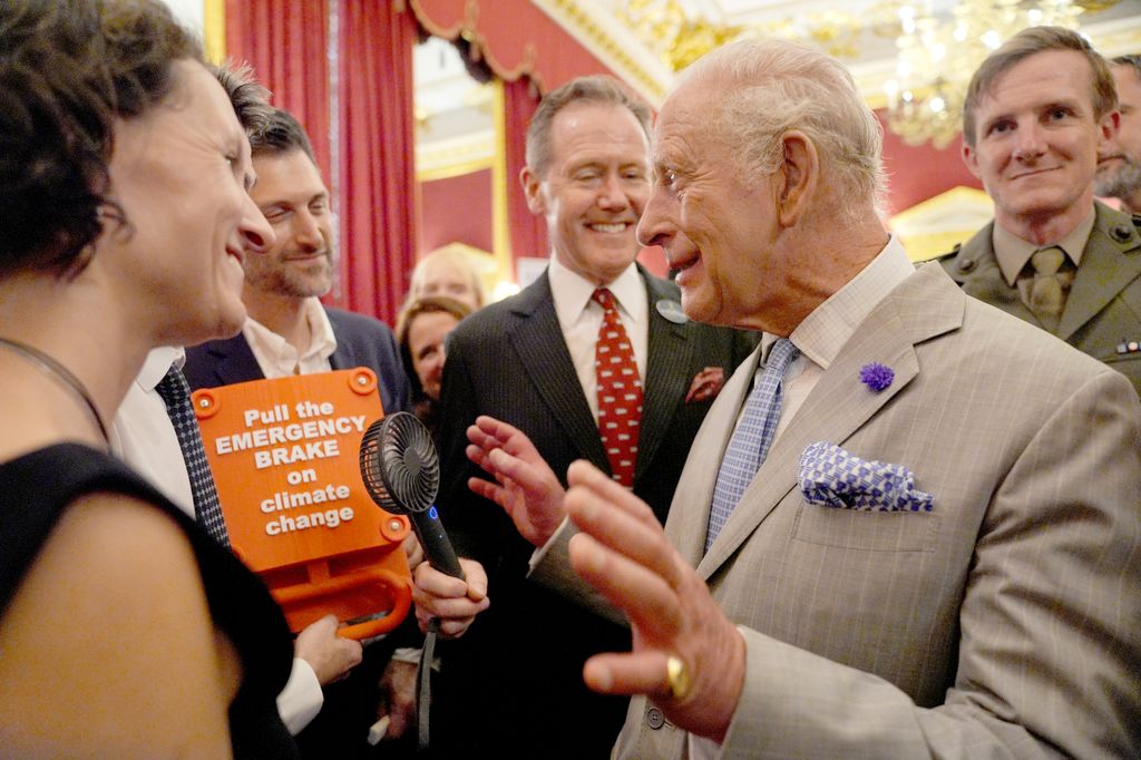 El vicealmirante Sir Tony Johnstone-Burt, jefe de la Casa del Rey, sostiene un pequeño ventilador portátil para el rey Carlos III durante la recepción de la Semana del Clima de Londres, organizada por el Departamento de Seguridad Energética y Cero Emisiones Netas (DESNZ), en el Palacio de St. James, en Londres, el 24 de junio de 2026