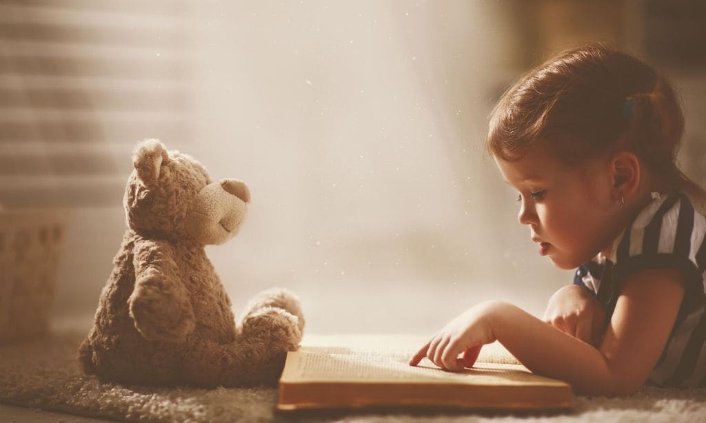 ni a leyendo un cuento con su osito de peluche