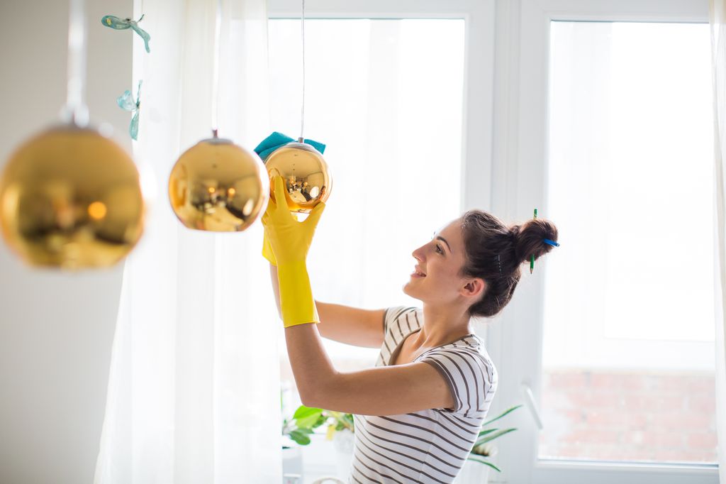 Mujer limpiando una lámpara con bayeta de microfibra. 