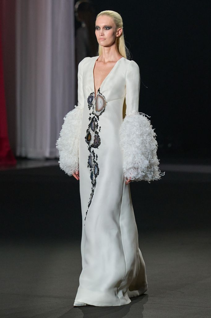 Modelo en pasarela con vestido blanco de mangas voluminosas y diseños geométricos.