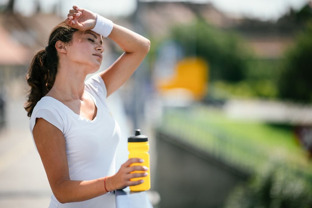 mujer cansada después de hacer ejercicio al aire libre, con una botella en la mano
