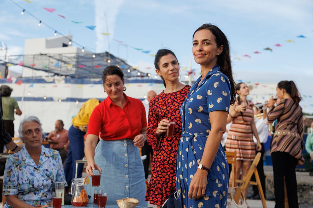 Paula Echevarría, con un vestido azul estampado, aparece junto a otras dos actrices durante una escena de fiesta de A la deriva