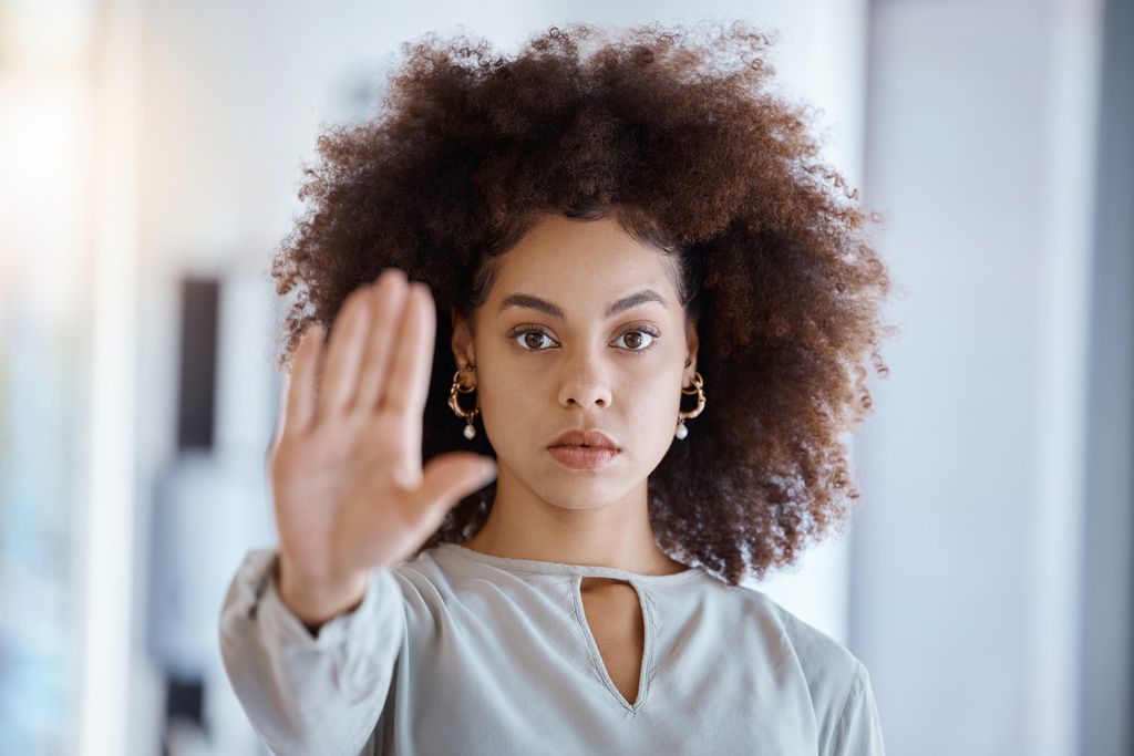 mujer con el pelo rizado mirando a cámara haciendo la señal de stop con su mano