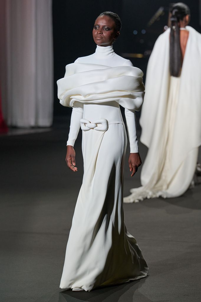 Modelo en pasarela con vestido blanco de manga larga y hombros acolchados.