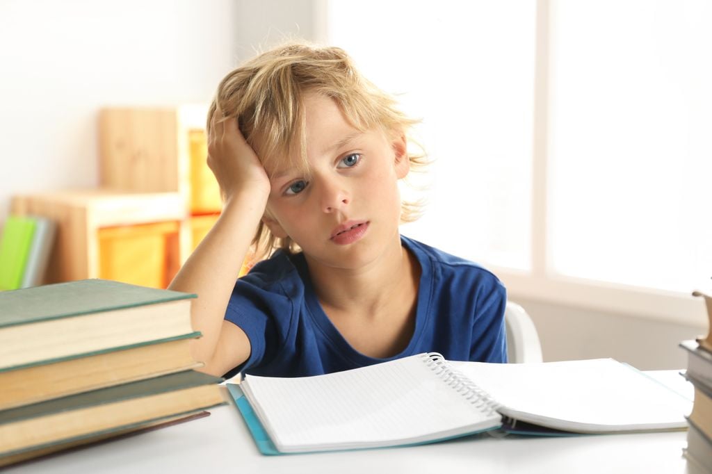 Niño con cara de cansado y tristeza sentado delante de los libros