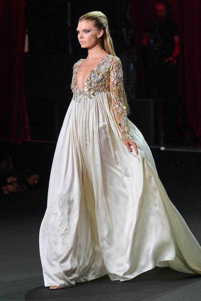 Modelo caminando en pasarela con vestido blanco y mangas doradas.
