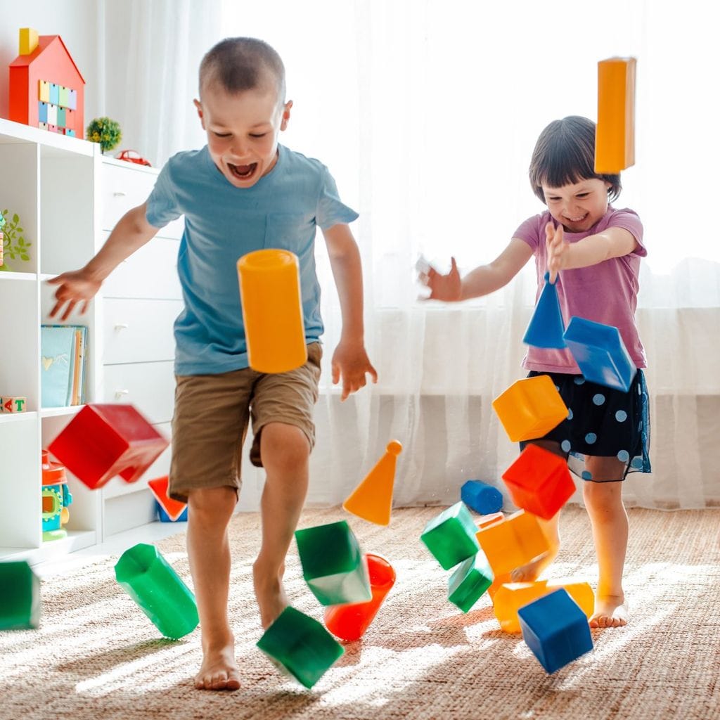 Niños jugando con juguetes en una habitación desordenada. Niños de Alta Demanda.