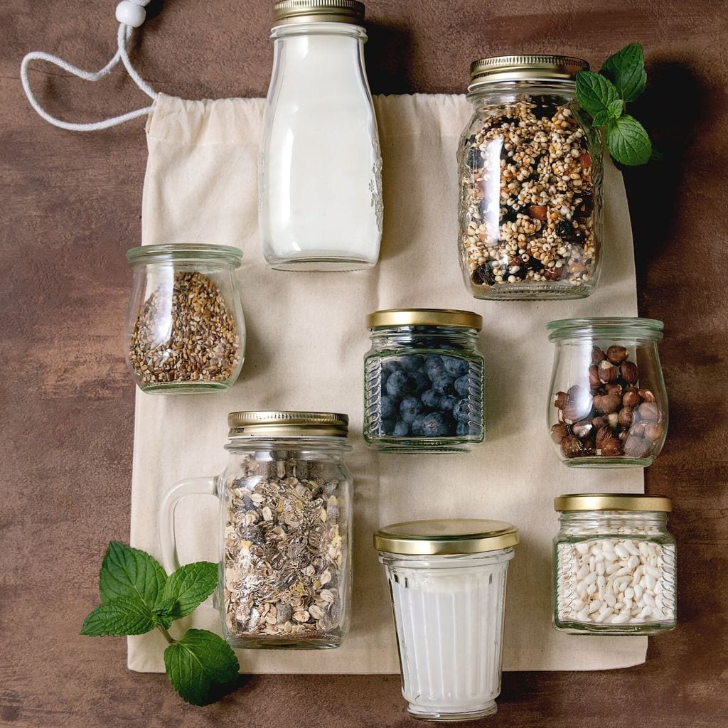 Homemade crunchy puffed millet grain granola with dried fruits and nuts. yogurt. milk. muesli in different glass jars on cotton bag. Brown background. Flat lay. Healthy food eco friendly breakfast
