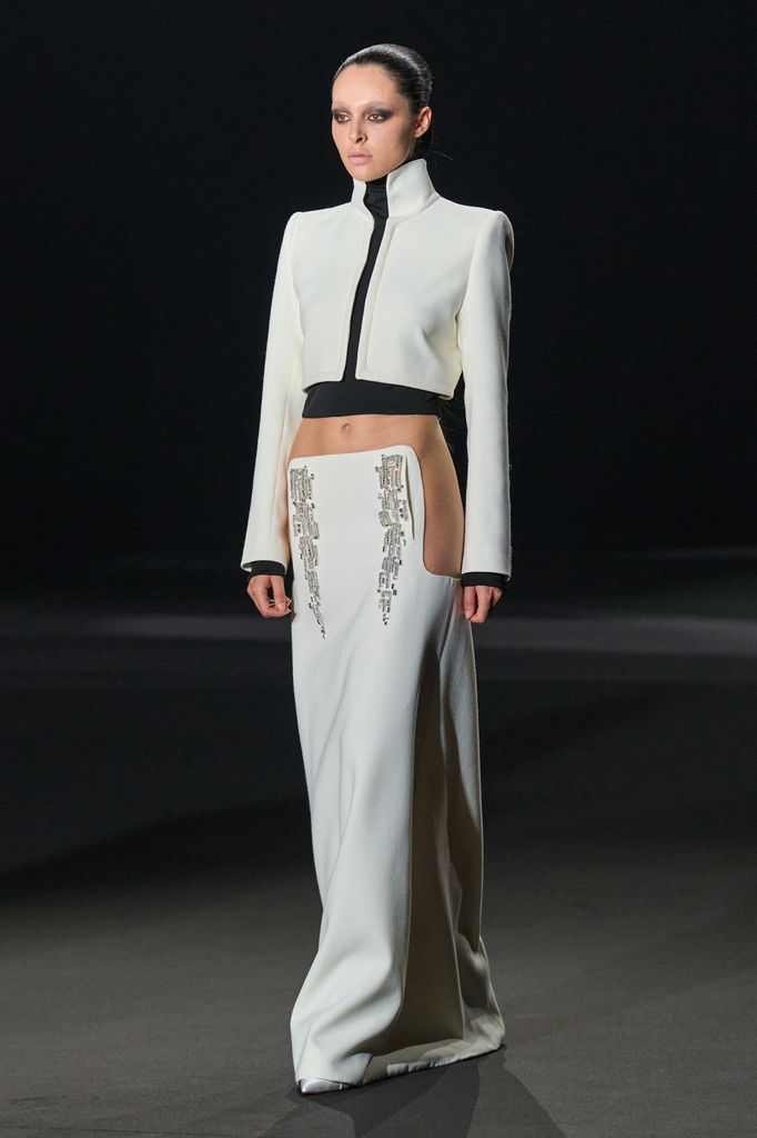 Modelo en pasarela con traje blanco de manga larga y falda larga.