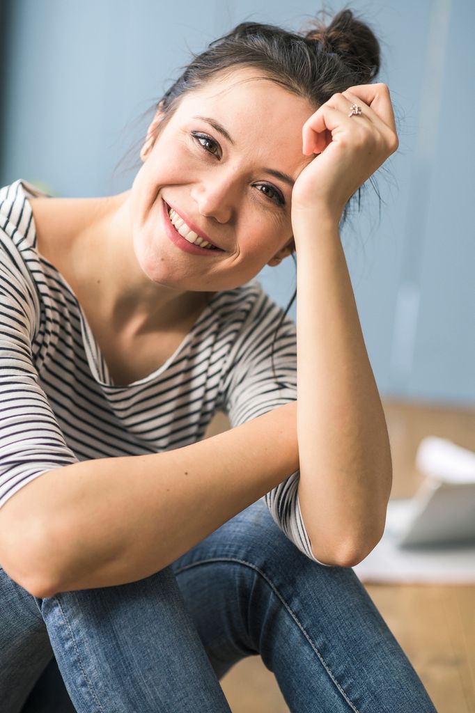mujer sonriente sentada, con la mano sujetando su cabeza