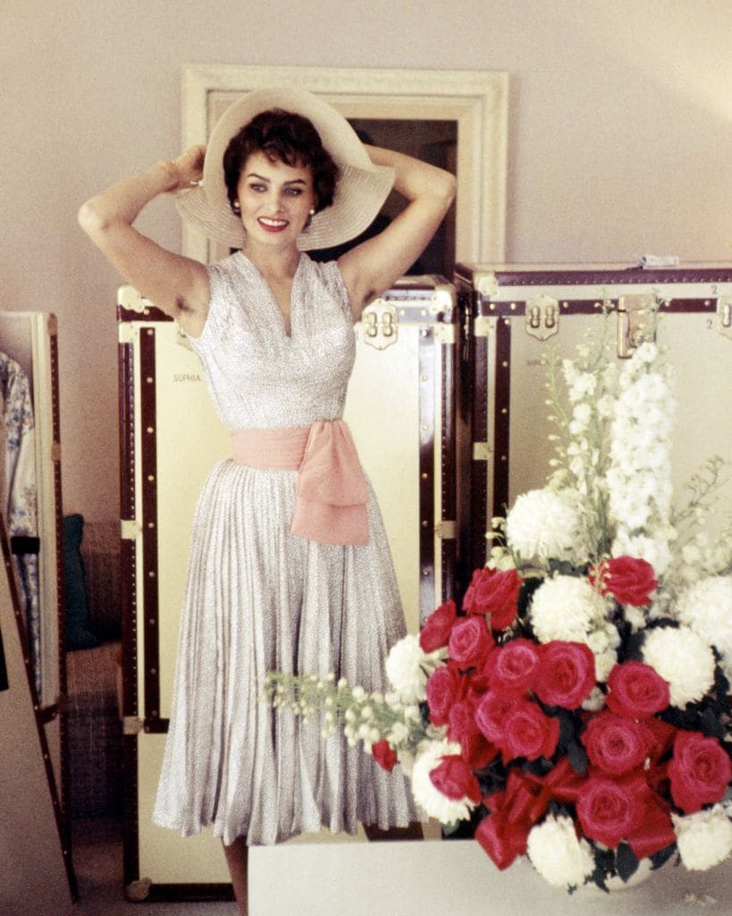 Sofia Loren posando con un vestido blanco y sonriendo mientras se pone un sombrero en una foto de archivo de 1955
