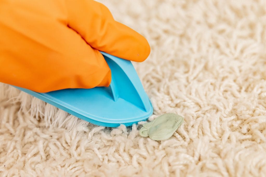 Persona quitando un chicle de la alfombra.