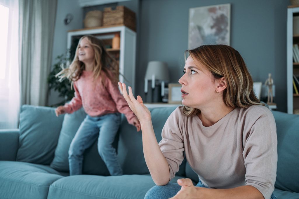 madre estresada con su hija saltando en el sofá