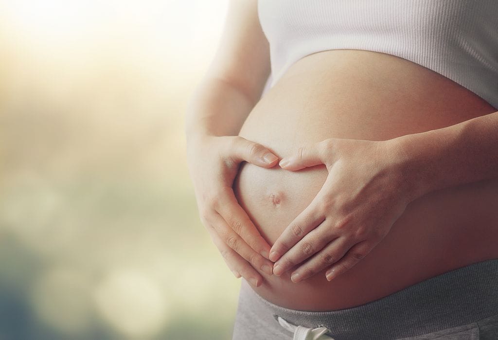 El vientre de la mujer embarazada con los dedos símbolo del corazón.