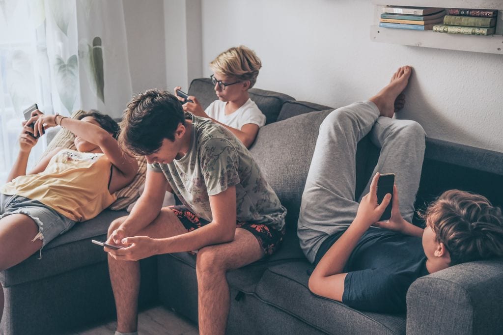 Hermanos usando todos el teléfono móvil en casa