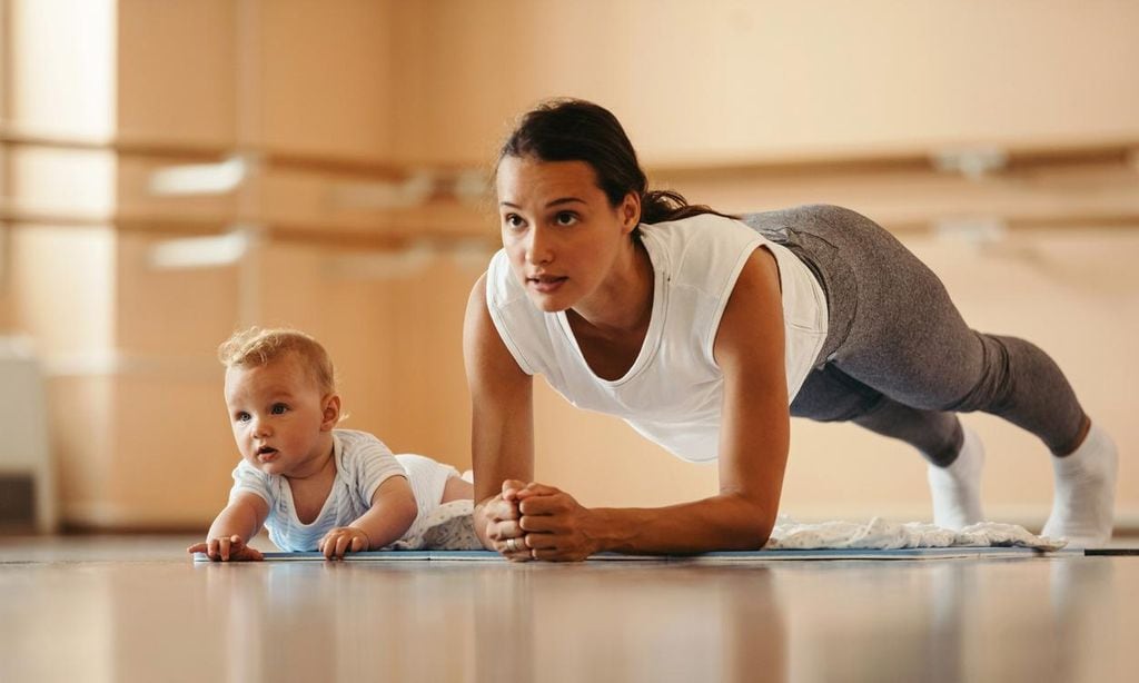 Mujer realiza plancha con su bebé al lado