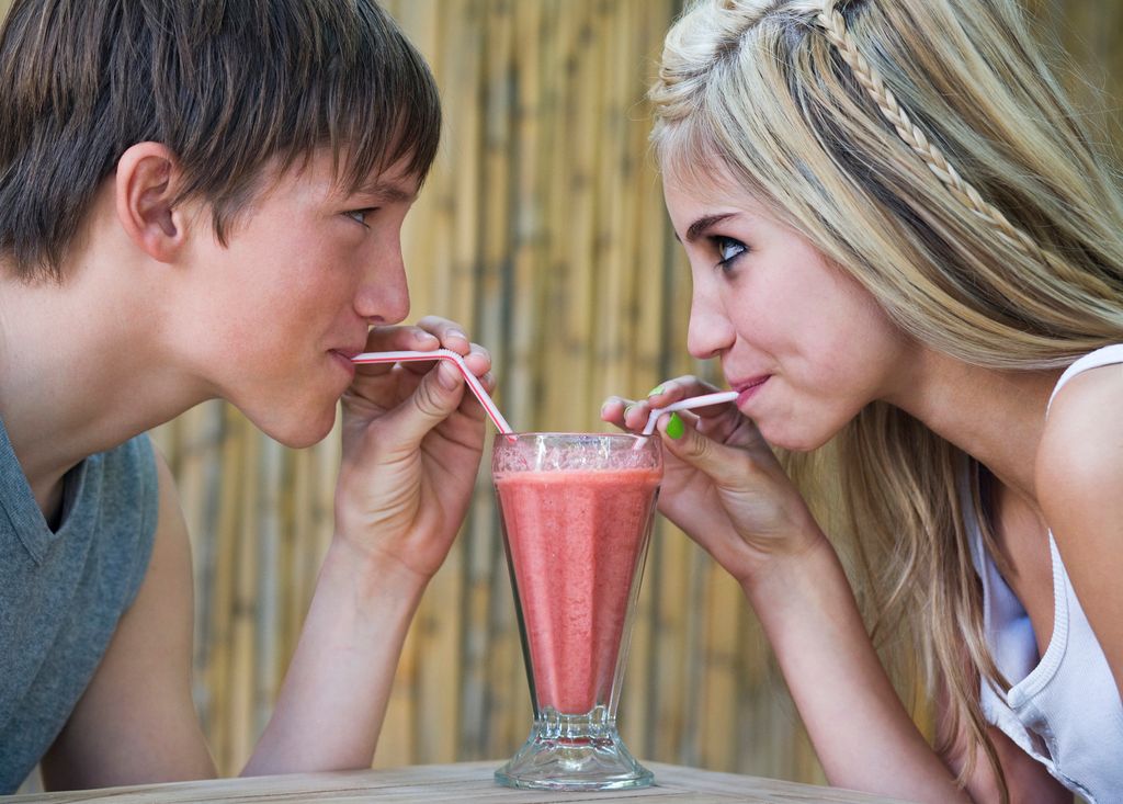 Adolescentes beben un batido del mismo vaso con pajitas