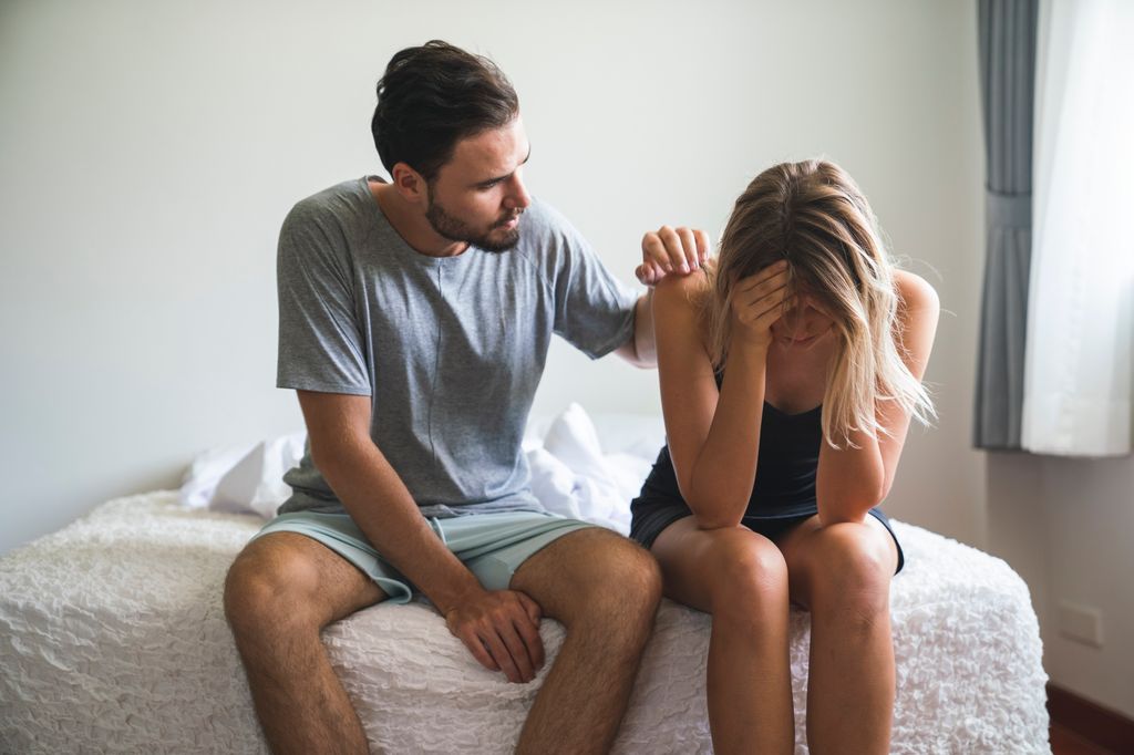 hombre consolando a su pareja, sentados en la cama