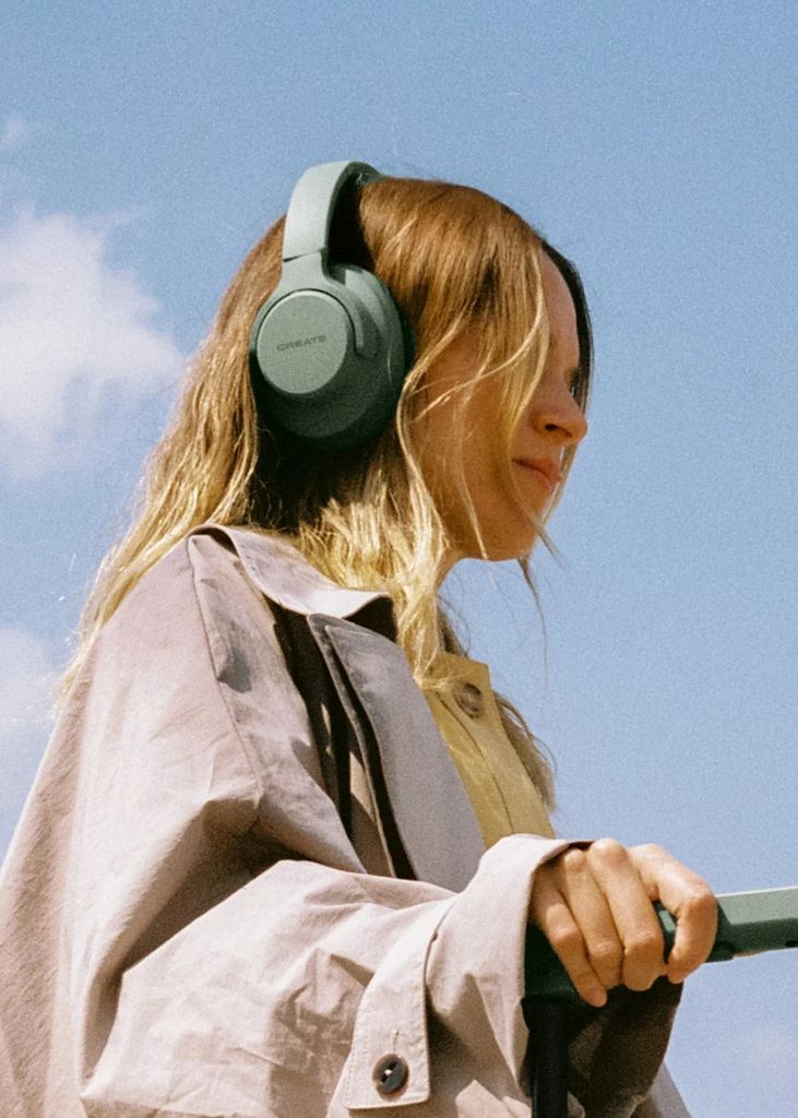 Chica escuchando música con unos auriculares de cancelación de ruido de diadema, en la calle, con ropa de otoño-invierno.