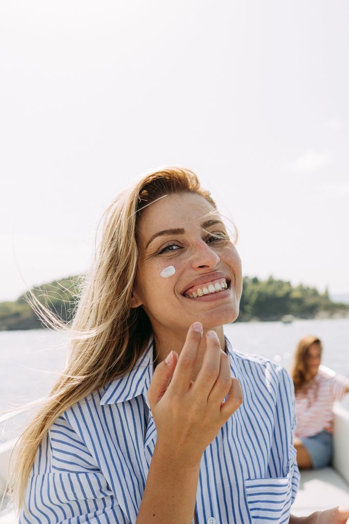 Photo of a smiling woman applying sunscreen while taking a boat ride with her friends