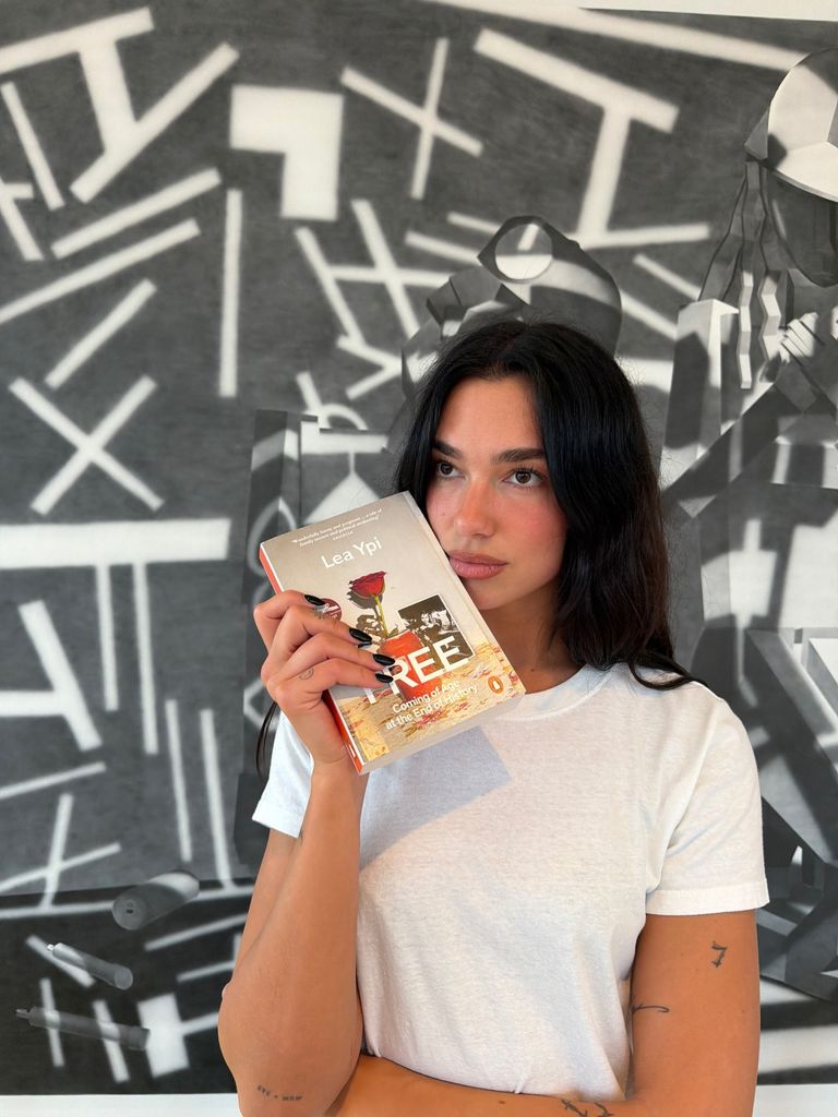 Dua Lipa con camiseta blanca de manga corta sosteniendo el libro Free de Lea Ypi