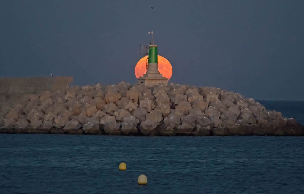 La superluna del Esturión asoma imponente tras el faro de la playa de San Andrés, en Málaga