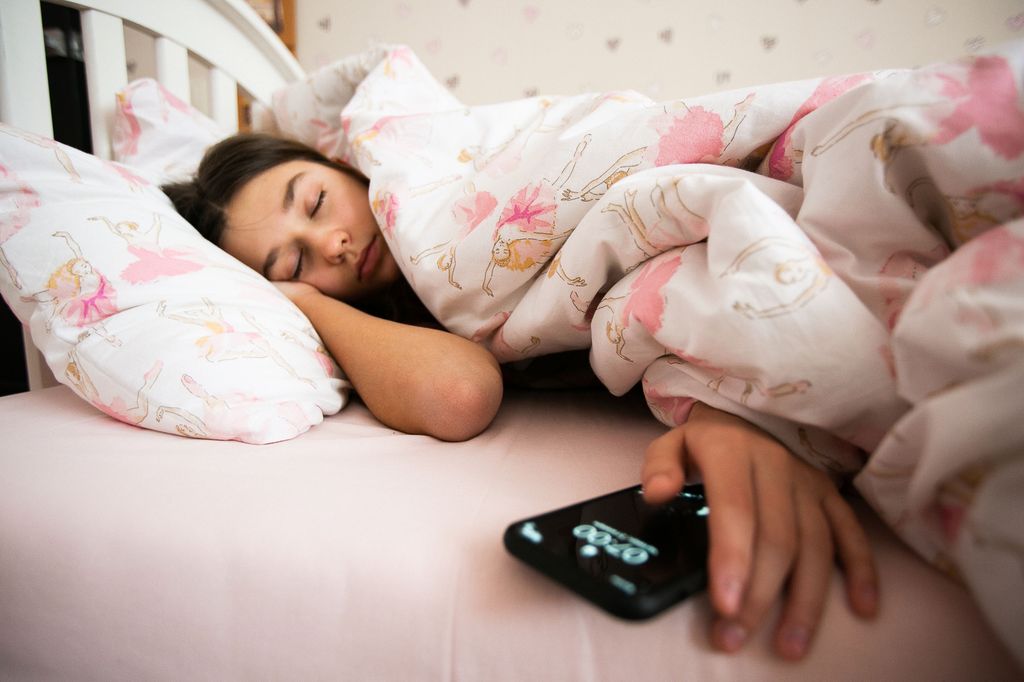 adolescente dormida en la cama, con el móvil en la mano