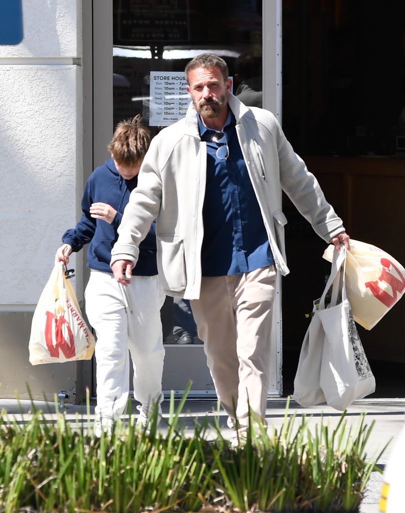 04/20/2025 Ben Affleck is pictured out shopping with his son Samuel on Easter Sunday in Los Angeles. The 52 year old American actor hit up Wold Market sporting a blue top and tan trousers. Ben could be seen discretely loading a  DC Batman Hush Version Figure into his car.