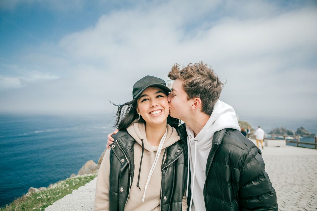 pareja de adolescentes dándose un beso junto al mar