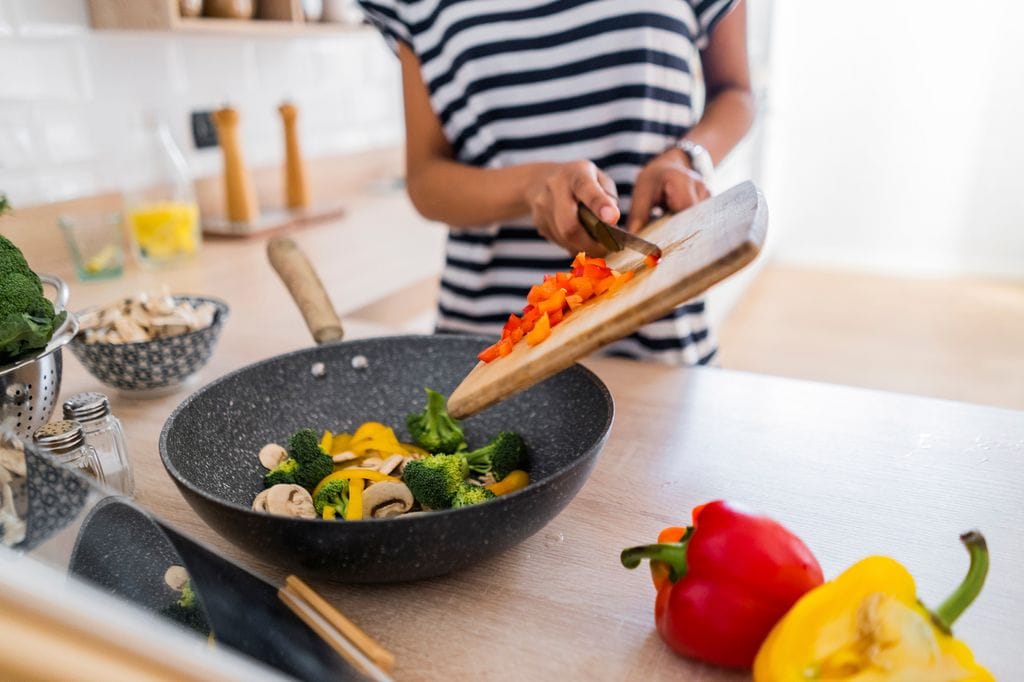 mujer cocinando verduras en una sartén