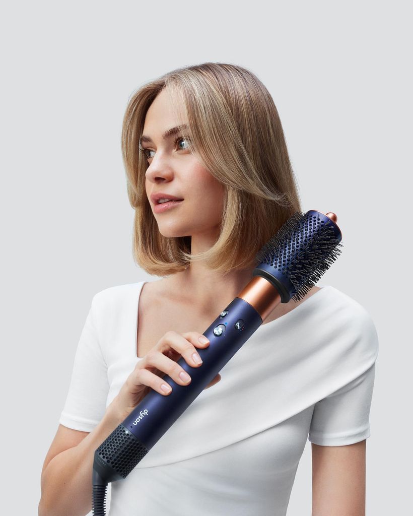 Mujer rubia con pelo corto peinándose con moldeador de Dyson