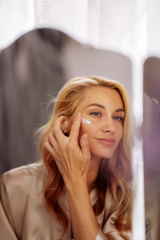 Mujer rubia aplicándose crema frente al espejo