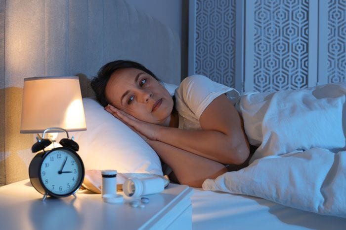 mujer en la cama con pastillas en la mesilla de noche